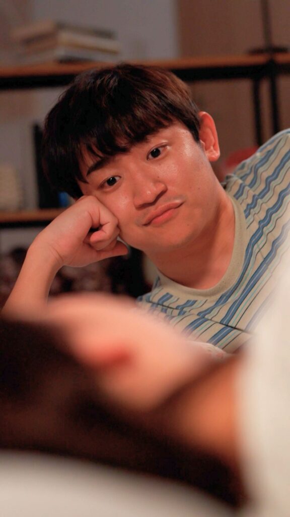 Close-up portrait of a man resting his head on his hand, looking at the camera with a calm expression, wearing a striped shirt.