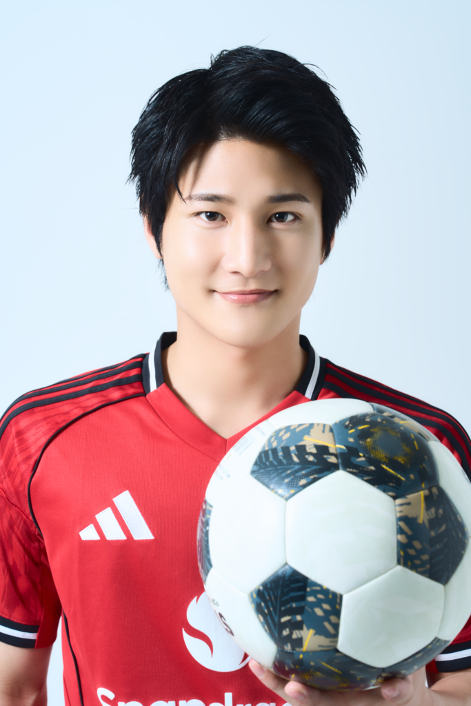 Young soccer player in a red jersey holding a patterned soccer ball against a light blue background.