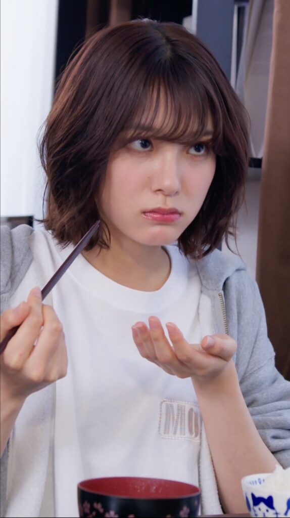 Woman with short brown hair looks to the side while holding a slim makeup tool near her face, indoors.