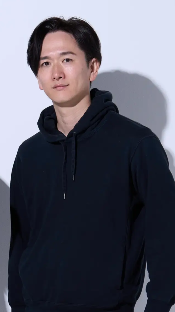 Portrait of a man in a black hoodie looking at the camera against a pale blue background.