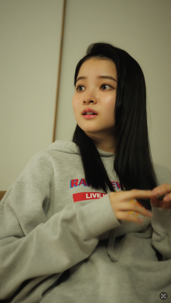 福島愛さま01 1 - 縦型ショートドラマなら GOKKO Inc.|ごっこ倶楽部 Young woman with long black hair in a gray hoodie, looking to her left.