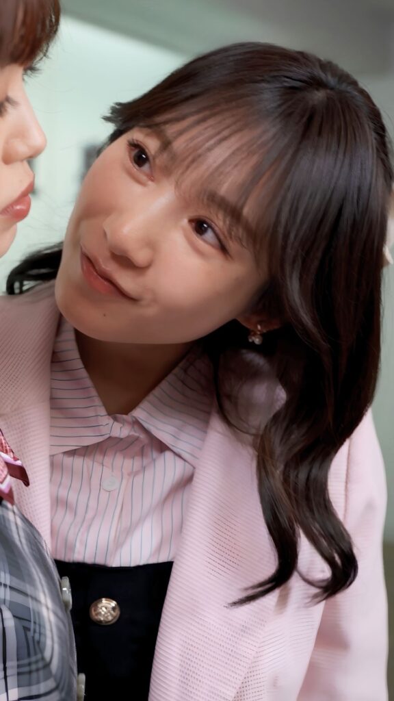 Close-up of a young woman in a light pink blazer and striped blouse, looking to the left and smiling at a person next to her.