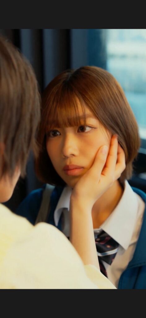 Close-up of a young woman in a school uniform being gently touched on the cheek by another person, her expression calm and thoughtful.