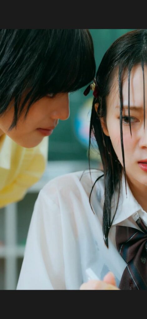 A boy in a yellow shirt leans in toward a girl in a white school uniform with a brown tie, as they stand close together.